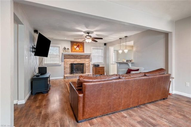 living area featuring baseboards, a ceiling fan, a brick fireplace, and wood finished floors