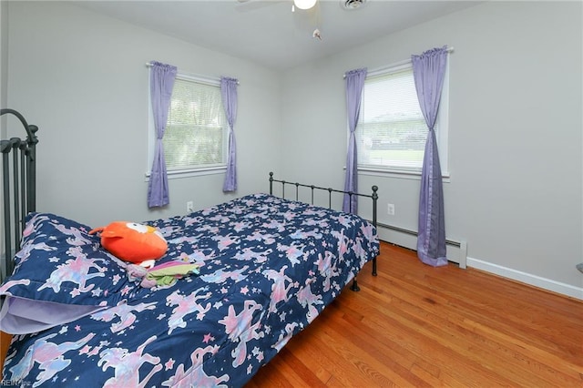 bedroom featuring a baseboard heating unit, wood finished floors, a ceiling fan, and multiple windows