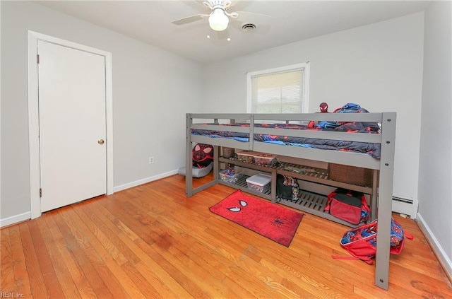 bedroom featuring hardwood / wood-style floors, baseboards, a baseboard radiator, and visible vents