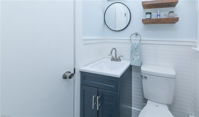 half bath with toilet, vanity, and a wainscoted wall