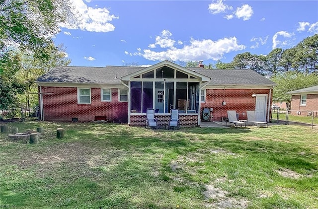 rear view of house featuring fence, a sunroom, a yard, and brick siding