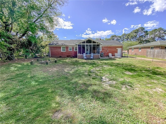 back of house featuring a lawn, a sunroom, fence, and brick siding