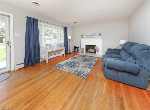 living room with a fireplace, wood finished floors, visible vents, and plenty of natural light