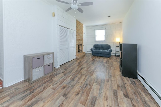 sitting room featuring baseboards, wood finished floors, ceiling fan, a fireplace, and a baseboard radiator