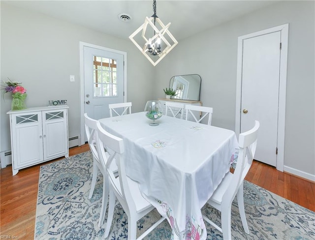 dining space with a baseboard heating unit, wood finished floors, a chandelier, and visible vents