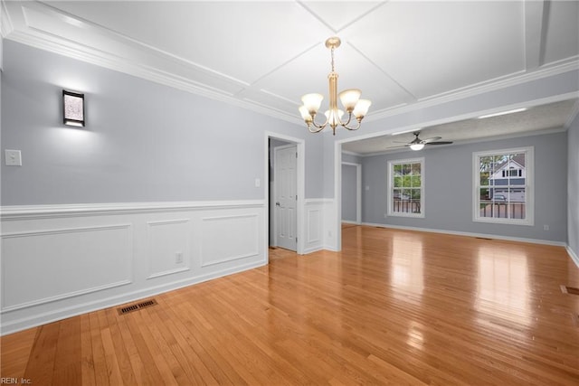 interior space with light wood finished floors, a wainscoted wall, visible vents, ceiling fan with notable chandelier, and ornamental molding