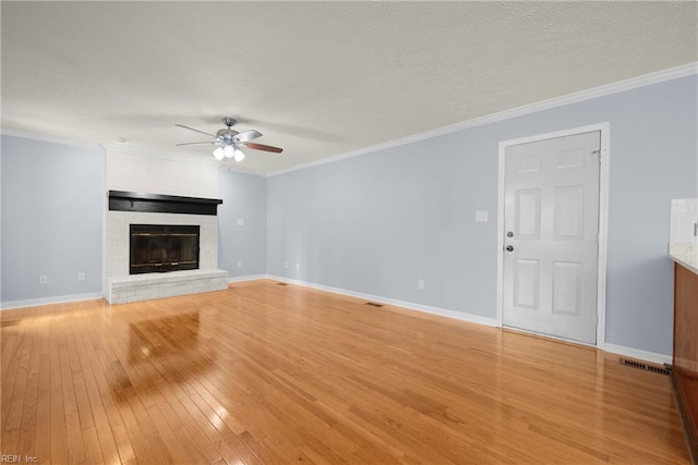 unfurnished living room with ceiling fan, ornamental molding, a brick fireplace, and light wood-style flooring