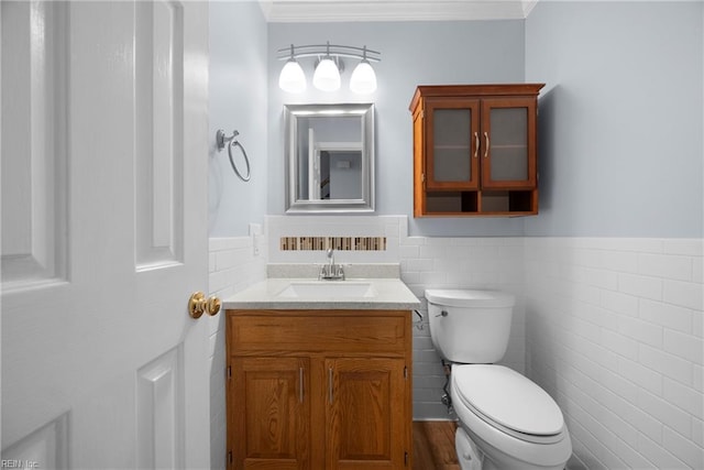 bathroom with vanity, tile walls, a wainscoted wall, toilet, and ornamental molding