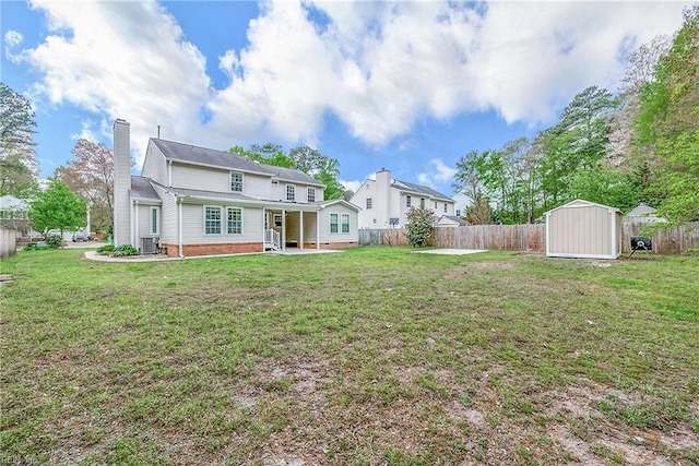 rear view of property featuring a lawn, a fenced backyard, a storage unit, and a chimney