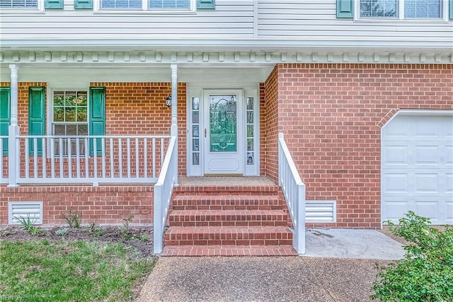 view of exterior entry with a porch, an attached garage, and brick siding