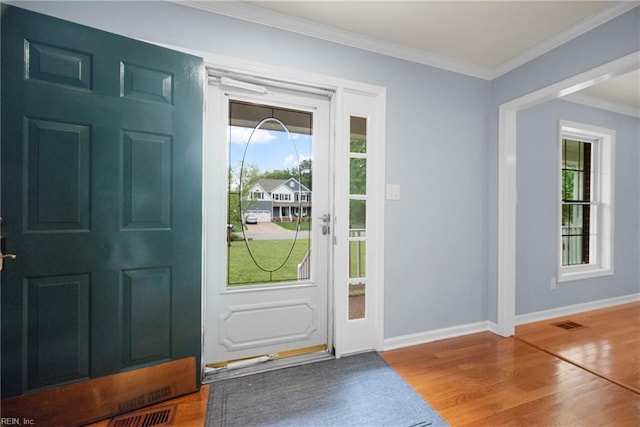 foyer entrance with baseboards, crown molding, wood finished floors, and visible vents