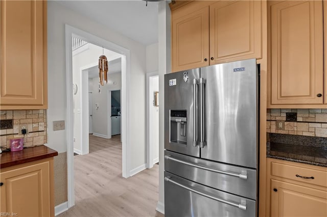 kitchen with dark stone counters, light wood-type flooring, baseboards, decorative backsplash, and stainless steel refrigerator with ice dispenser