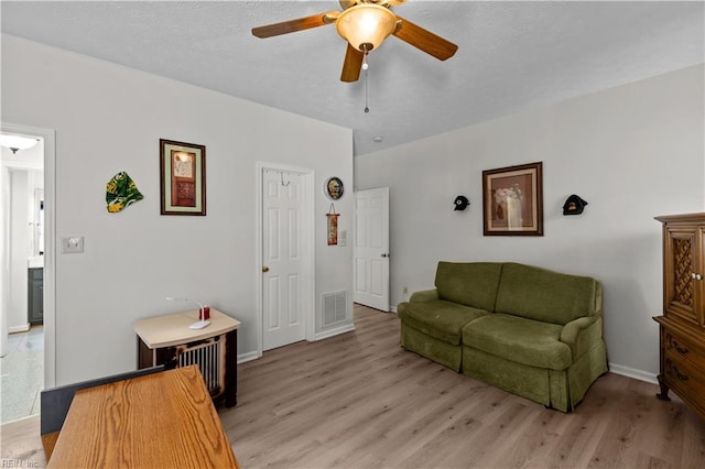 living area featuring light wood-style floors, visible vents, a ceiling fan, and baseboards