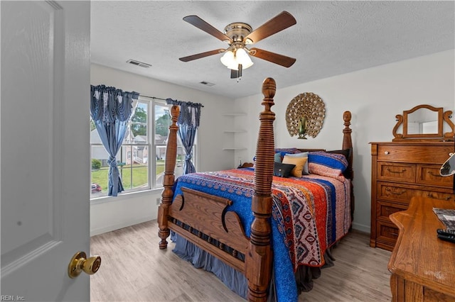 bedroom with wood finished floors, a textured ceiling, a ceiling fan, and visible vents