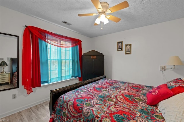 bedroom with a textured ceiling, visible vents, baseboards, wood finished floors, and ceiling fan