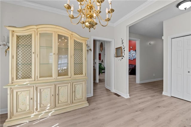 unfurnished dining area featuring light wood-style floors, crown molding, baseboards, and an inviting chandelier