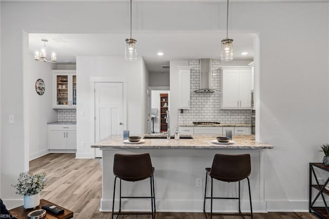 kitchen featuring white cabinets, tasteful backsplash, wood finished floors, wall chimney range hood, and a breakfast bar