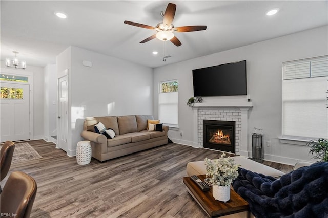 living area featuring ceiling fan with notable chandelier, a brick fireplace, wood finished floors, and recessed lighting