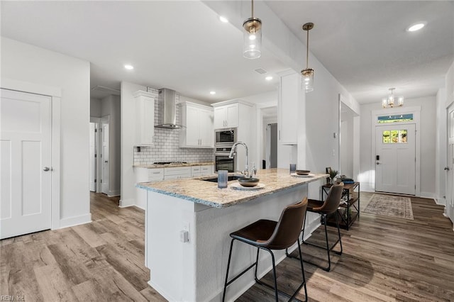 kitchen with wall chimney range hood, a sink, light wood-style floors, appliances with stainless steel finishes, and white cabinetry