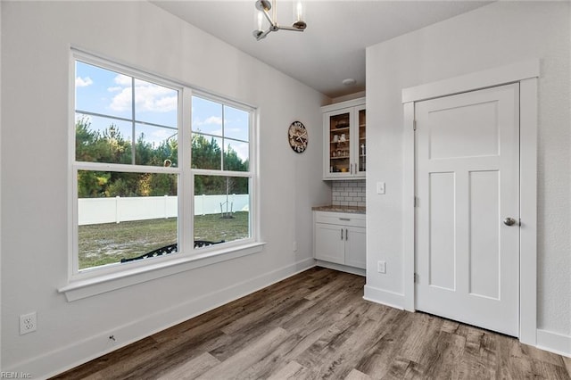unfurnished dining area featuring baseboards, an inviting chandelier, wood finished floors, and plenty of natural light