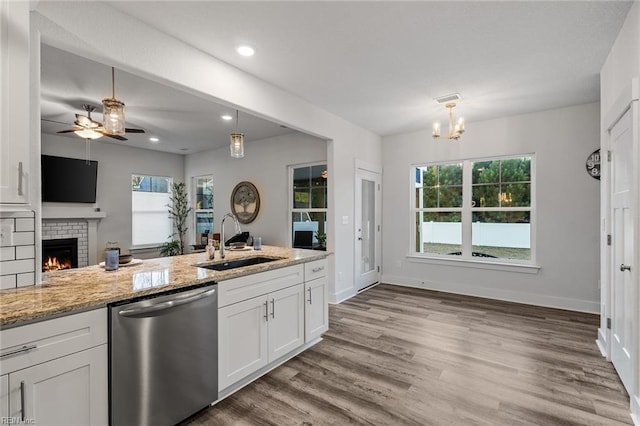 kitchen with a sink, ceiling fan with notable chandelier, dishwasher, a fireplace, and white cabinets
