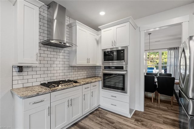 kitchen featuring dark wood-style floors, wall chimney exhaust hood, tasteful backsplash, appliances with stainless steel finishes, and white cabinetry