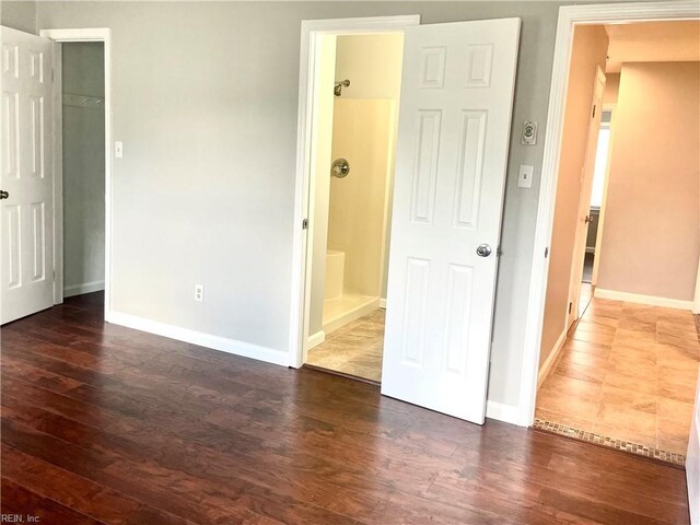 unfurnished bedroom with baseboards, a spacious closet, a closet, ensuite bath, and dark wood-type flooring
