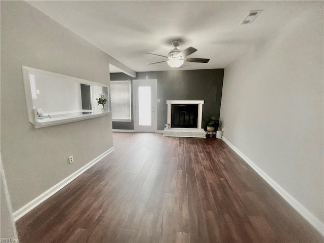 unfurnished living room with dark wood finished floors, visible vents, baseboards, a glass covered fireplace, and ceiling fan
