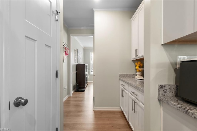 hall with light wood-style flooring, baseboards, and crown molding