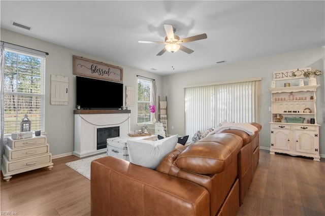 living area with wood finished floors, a glass covered fireplace, ceiling fan, baseboards, and visible vents