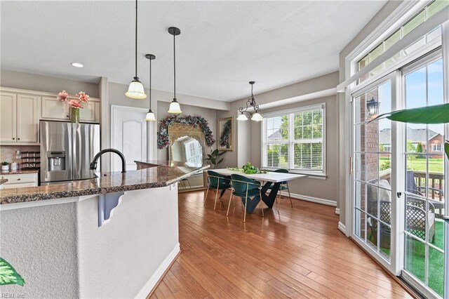 kitchen featuring light wood finished floors, stainless steel fridge, dark stone counters, baseboards, and hanging light fixtures