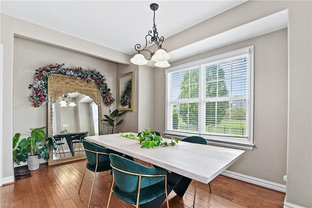 dining space featuring wood-type flooring, an inviting chandelier, and baseboards