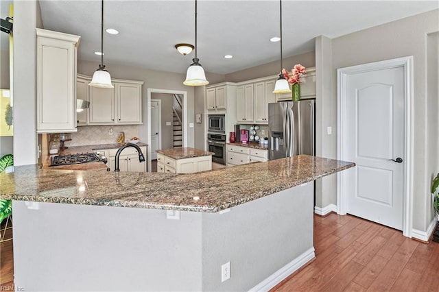 kitchen featuring wood finished floors, a sink, stone countertops, and appliances with stainless steel finishes