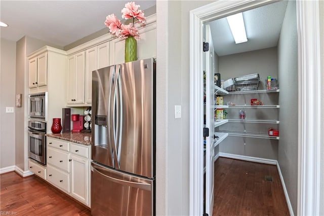 kitchen with white cabinets, baseboards, appliances with stainless steel finishes, and dark wood-style flooring