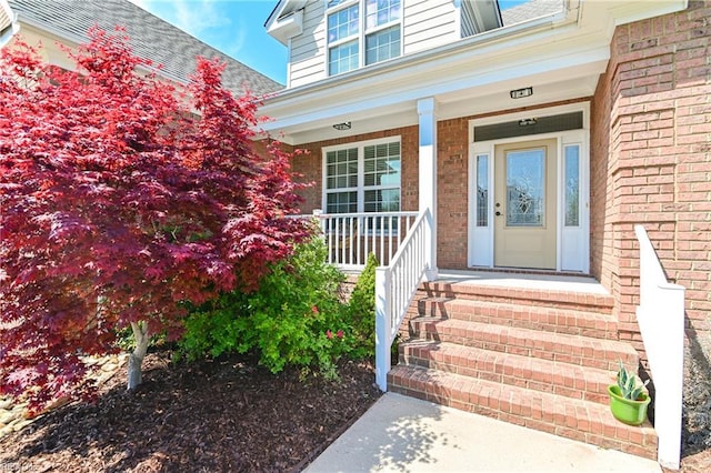 view of exterior entry featuring covered porch and brick siding