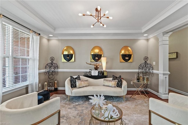 living area with a tray ceiling, an inviting chandelier, ornate columns, wood finished floors, and ornamental molding