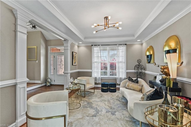 living area featuring ornate columns, a tray ceiling, wood finished floors, ornamental molding, and a chandelier