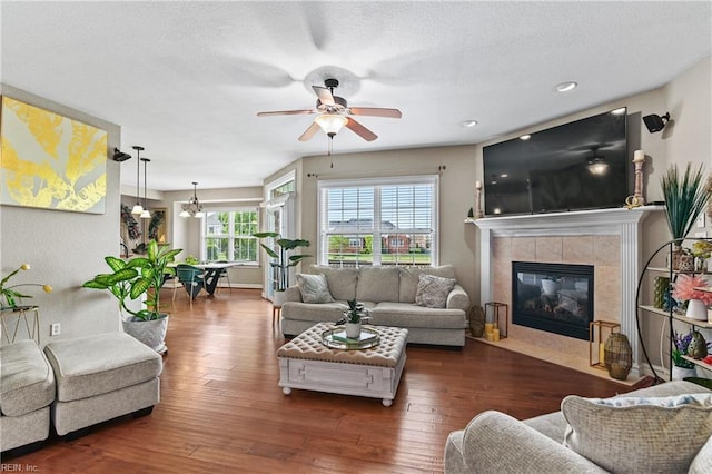 living room featuring a tile fireplace, a textured ceiling, hardwood / wood-style flooring, and ceiling fan