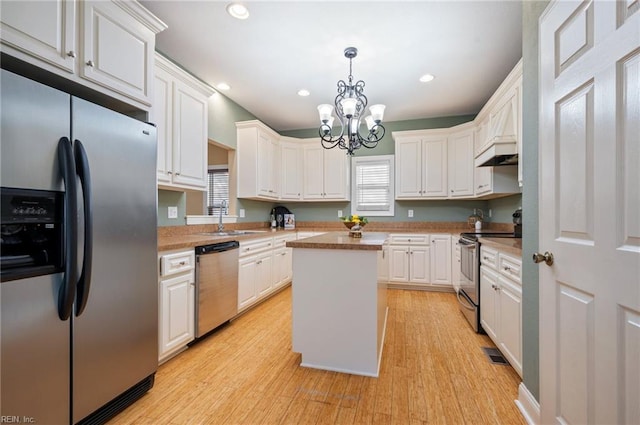 kitchen with stainless steel appliances, a sink, light wood-type flooring, white cabinetry, and a kitchen island