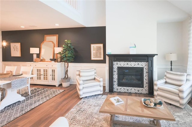 living room with a decorative wall, wood finished floors, a tile fireplace, and wainscoting