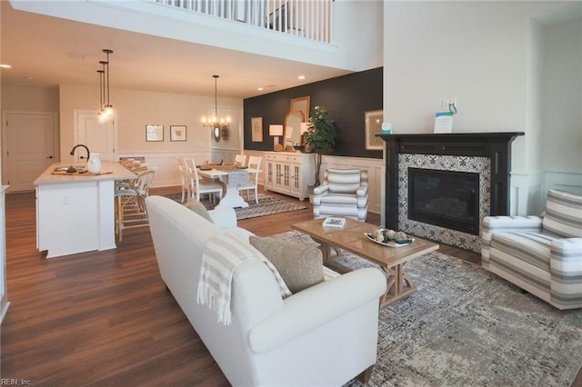 living room featuring wainscoting, a tiled fireplace, a chandelier, and dark wood finished floors