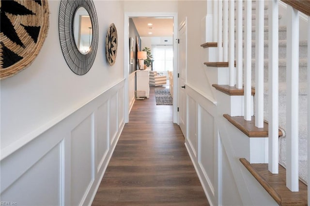 corridor with stairway, a decorative wall, dark wood-style flooring, and wainscoting