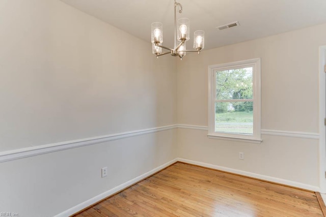 empty room featuring a chandelier, visible vents, light wood finished floors, and baseboards