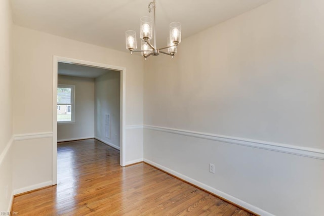 spare room with baseboards, light wood-style floors, and a notable chandelier