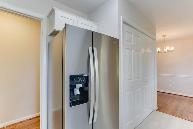 kitchen with light wood-style flooring, baseboards, white cabinets, stainless steel refrigerator with ice dispenser, and a notable chandelier