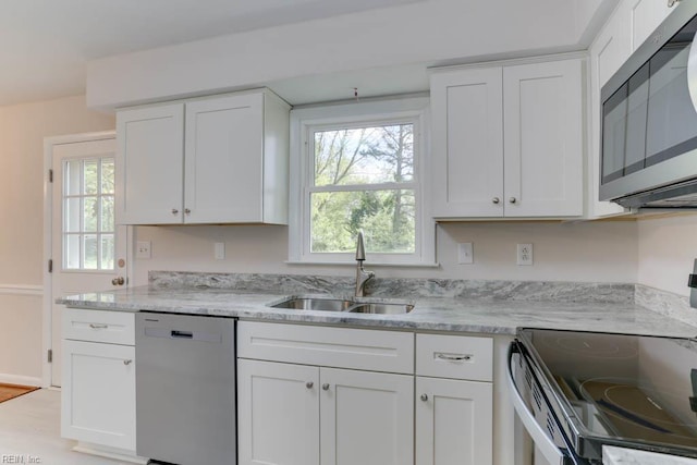 kitchen featuring light stone counters, white cabinets, appliances with stainless steel finishes, and a sink