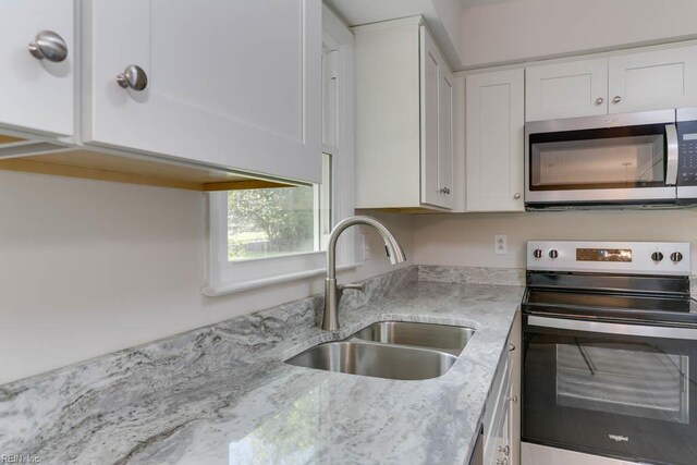 kitchen featuring light stone counters, white cabinetry, stainless steel appliances, and a sink