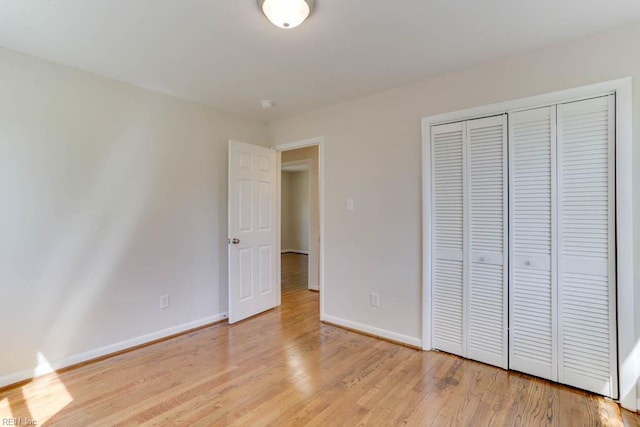 unfurnished bedroom featuring light wood finished floors, baseboards, and a closet