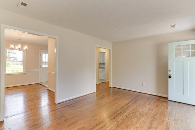 spare room featuring light wood-style flooring, visible vents, baseboards, and an inviting chandelier