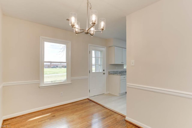 unfurnished dining area with an inviting chandelier, light wood finished floors, and baseboards